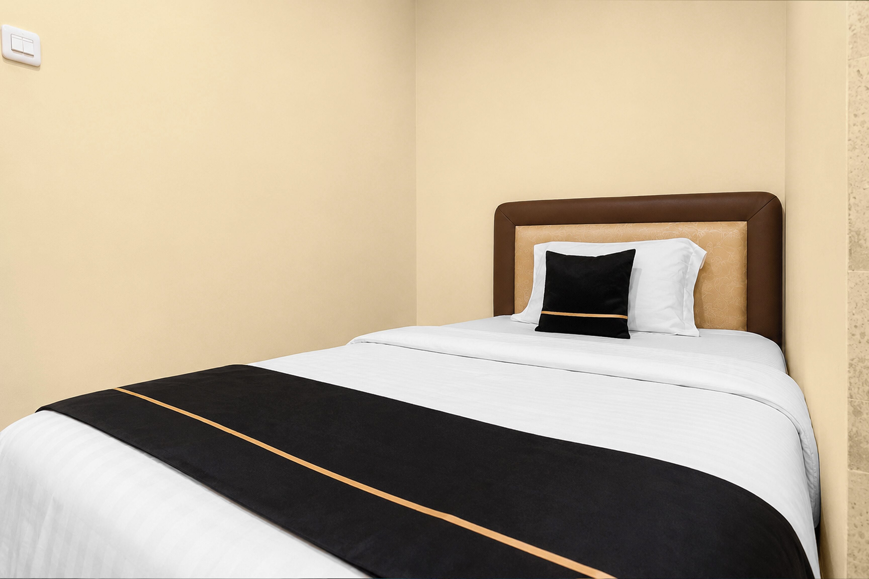 A neatly made bed with a white and black bedspread, a brown headboard, and a single black pillow.