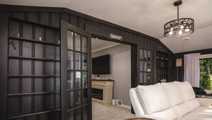 Een kamer met een witte bank, een ronde houten salontafel, een tv met een zwarte lijst en een kroonluchter.