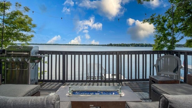 Een terras met buitenmeubilair, een barbecue en uitzicht op een meer.