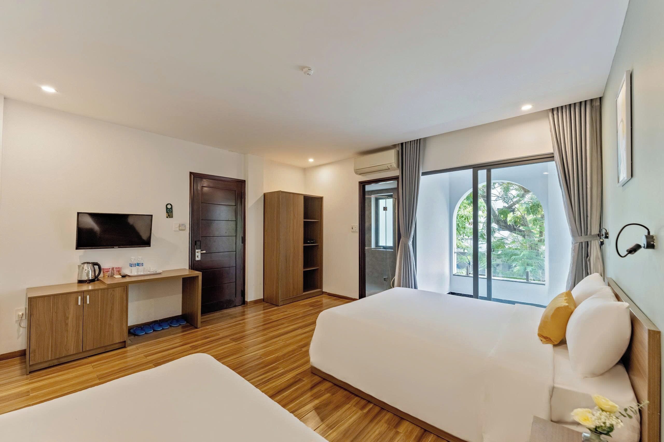 A hotel room with two beds, a TV, a desk with a kettle, and a wardrobe.