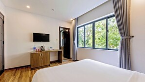 Una habitación de hotel con cama, escritorio, televisor y ventana con cortinas.