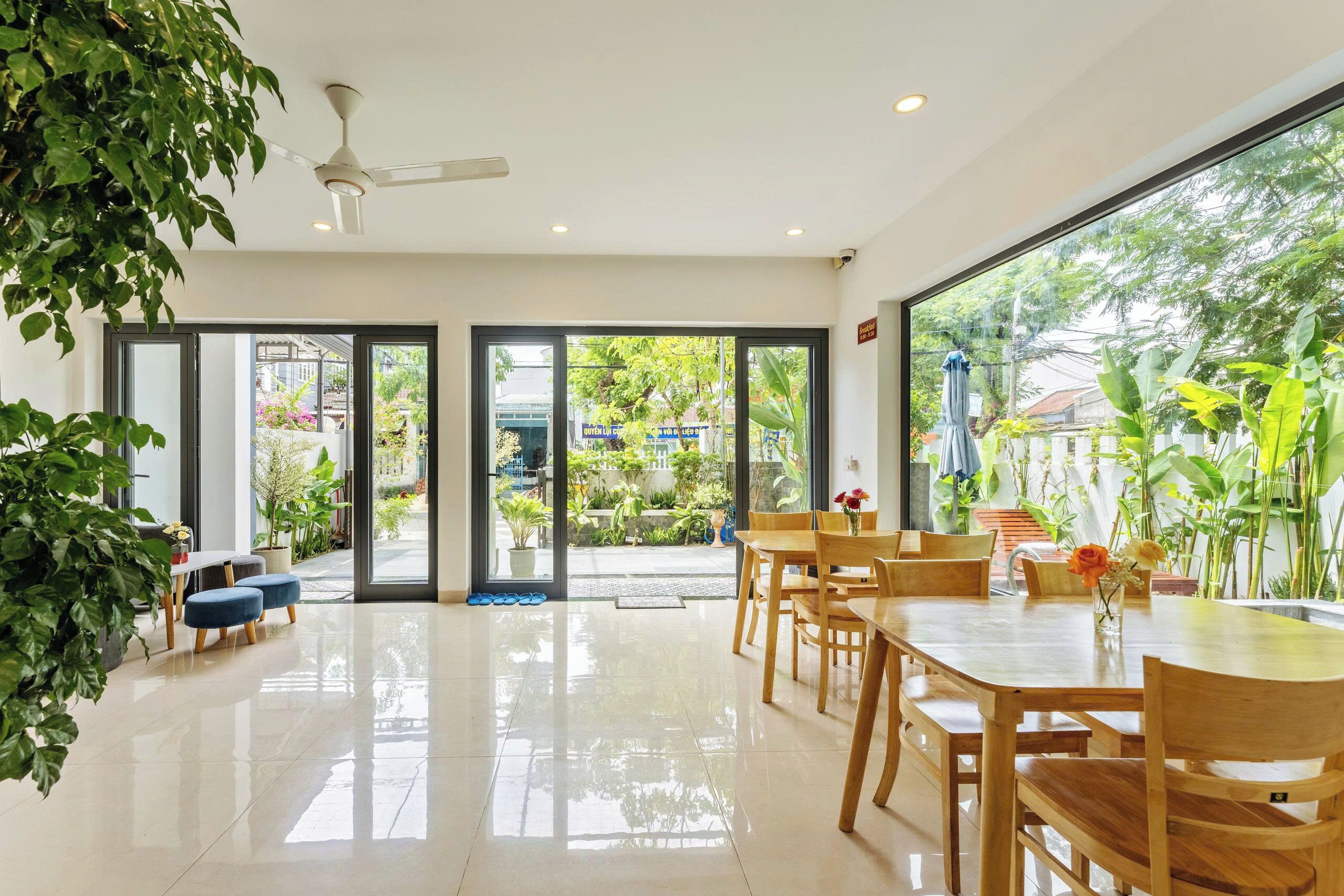 Amplia habitación con una gran mesa de comedor, sillas, un ventilador de techo y vista a un jardín a través de puertas de vidrio.