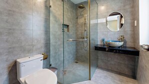 Un baño moderno con ducha envuelta en cristal, inodoro y lavamanos con recipiente.