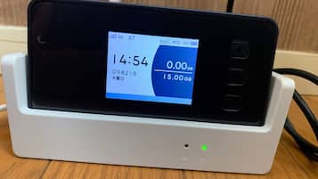 Un teléfono inteligente cargándose sobre una base blanca, mostrando la hora, el estado de la batería y la señal de la red.