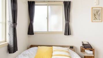 Un dormitorio con cama, cortinas, aire acondicionado, una mesita de noche con lámpara y un cuadro en la pared.