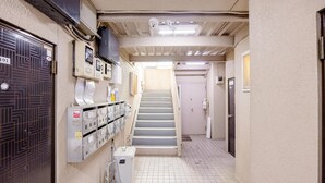 Un couloir étroit avec un escalier menant à une porte, une pièce utilitaire avec des casiers et une poubelle.