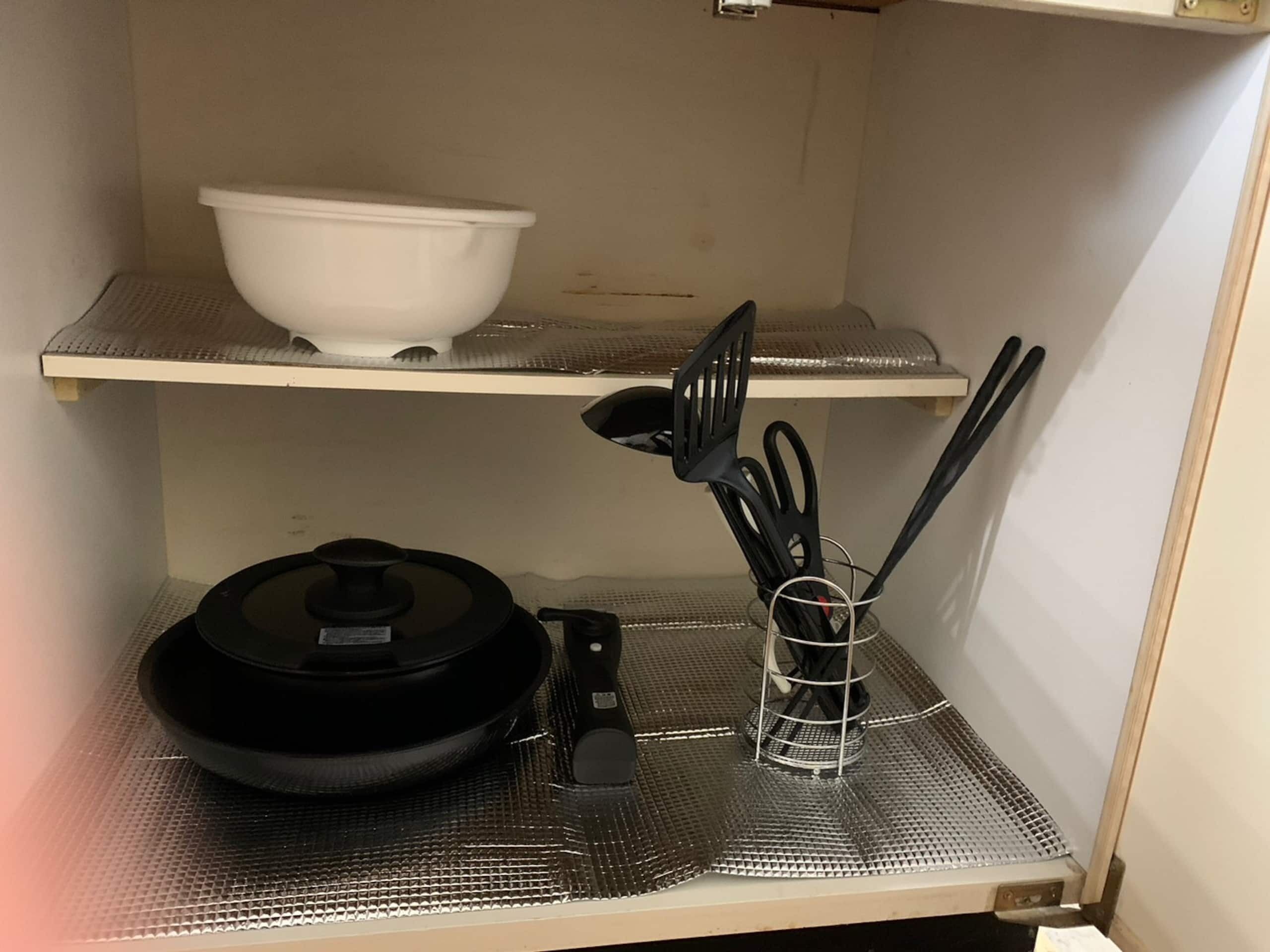 A kitchen with a black pot on a tray, a white bowl on a shelf, and a utensil holder with black utensils.