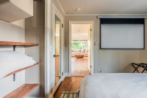 Ein Schlafzimmer mit einem Bett, einem Fernseher, einer Holzregal und einer Tür zu einem Wohnbereich.