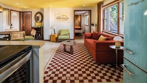 Ein wohnzimmer im Retro-Stil mit Schachbrettmuster auf dem Boden, einer Couch, einem Esstisch und einer Küchenzeile mit Kühlschrank.