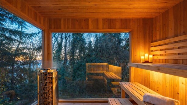 Ein Holz-Saunaraum mit einer Bank, einer Saunaheizung und Blick auf einen Wald.