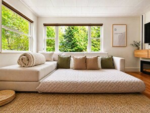 Ein modernes Wohnzimmer mit einem Ecksofa, einem großen Fenster mit Blick auf Bäume und einem flachbildfernseher an der Wand.