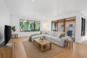 Una sala moderna con un sofá modular, un televisor de pantalla plana, una mesa de centro de madera y un ventanal con vistas a zonas verdes.