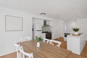 Una cocina moderna con armarios blancos, una isla central y un comedor con mesa de madera y sillas blancas.