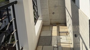 Un balcon étroit avec une balustrade noire, un sol carrelé et une fenêtre à cadre noir.