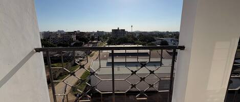 Un balcon doté d’une rambarde en métal, donnant sur un parking et des immeubles.
