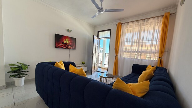 Un salon avec un canapé, un ventilateur de plafond, un téléviseur et une fenêtre avec des rideaux.