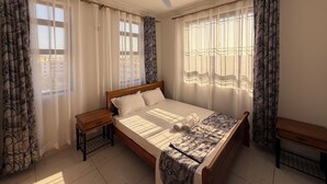 Une chambre à coucher avec un lit, un ventilateur de plafond, deux tables de chevet et des rideaux.