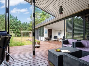Een modern terras buiten met rieten meubilair, een schommel en uitzicht op een bebost gebied.