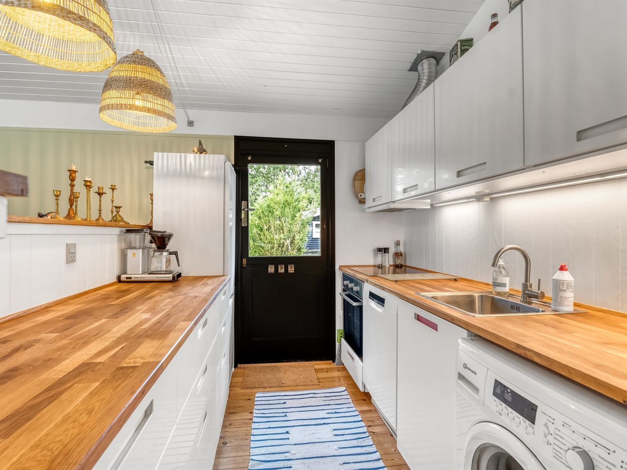 A compact kitchen with wooden countertops, a washing machine, and a black door leading outside.