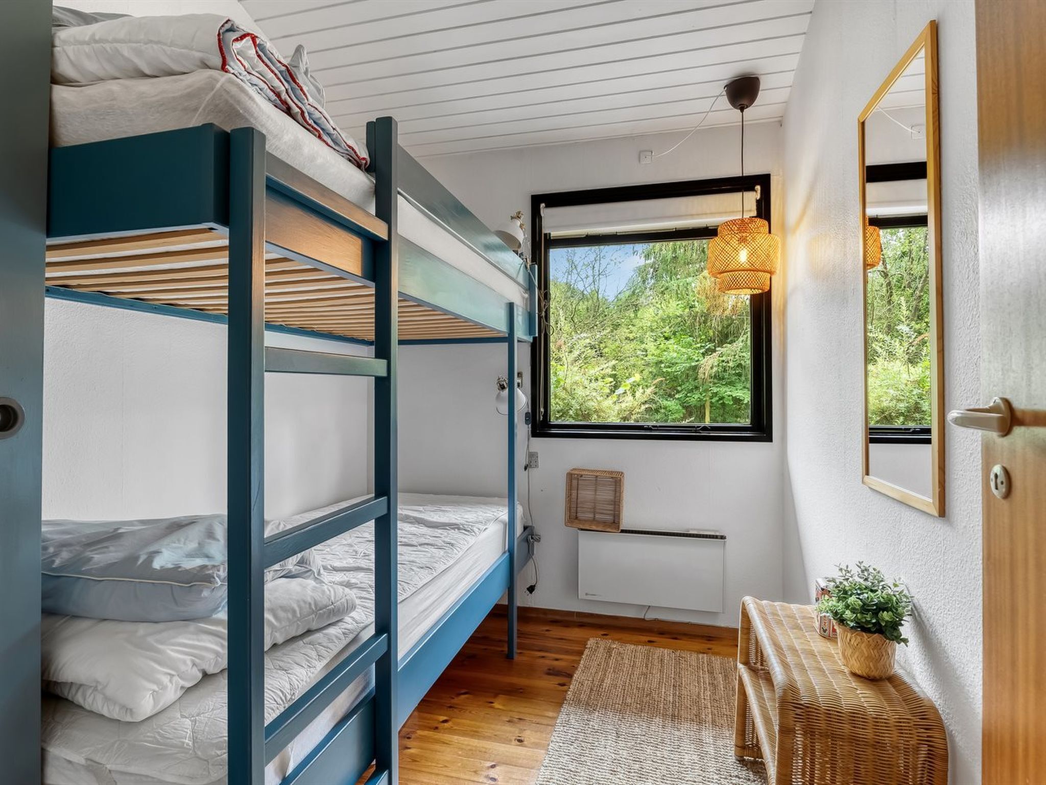 A bunk bed room with a window, a wicker side table, and a mirror on the wall.
