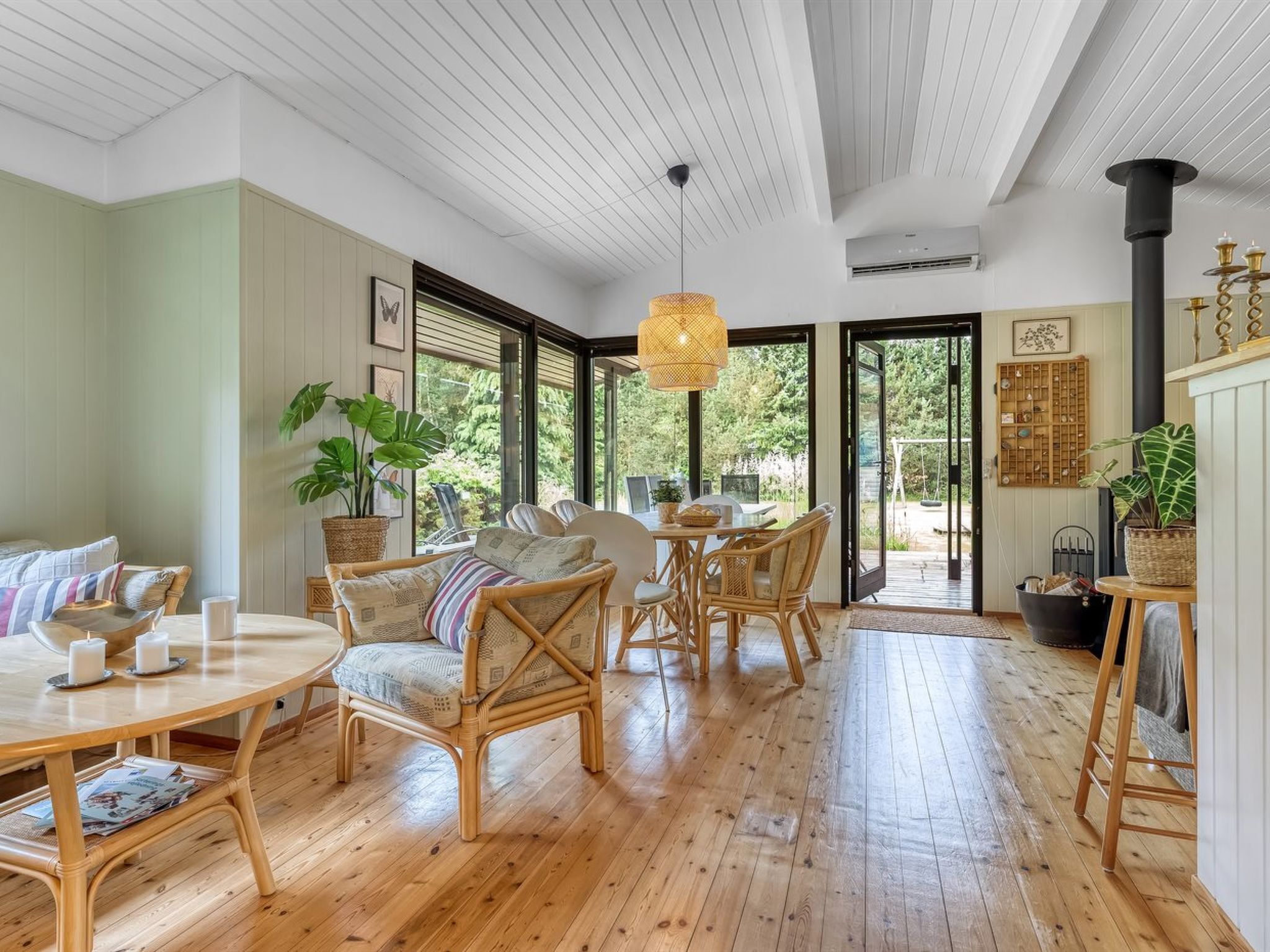 Amplia habitación con piso de madera, mobiliario de mimbre y grandes ventanas que ofrecen vistas al exterior.
