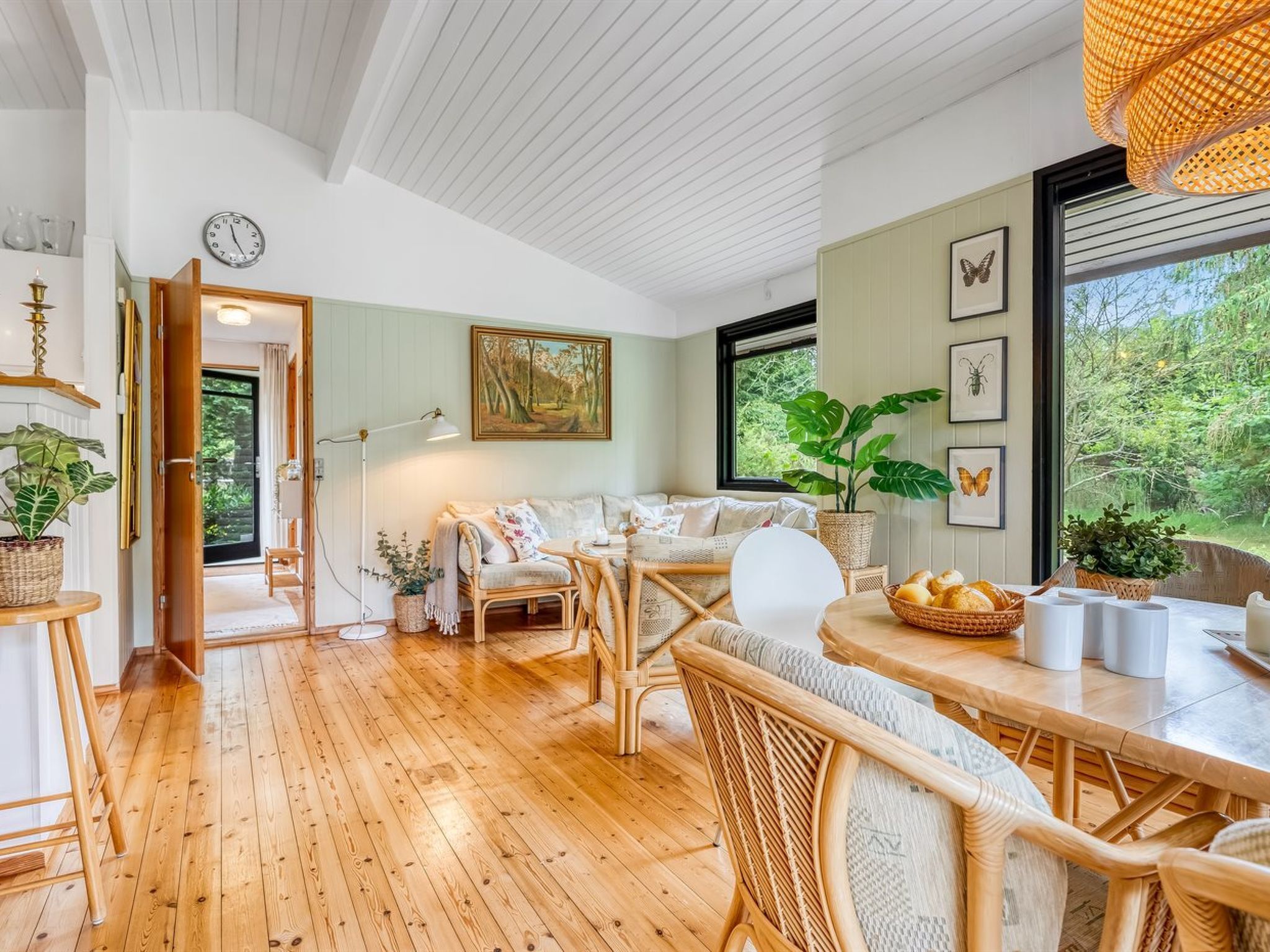 Une pièce chaleureuse avec un plancher en bois, une table à manger avec des chaises, un canapé et une grande fenêtre donnant sur un paysage verdoyant.