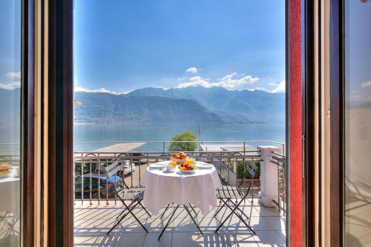 A balcony with a table set for breakfast, overlooking a lake and mountains.
