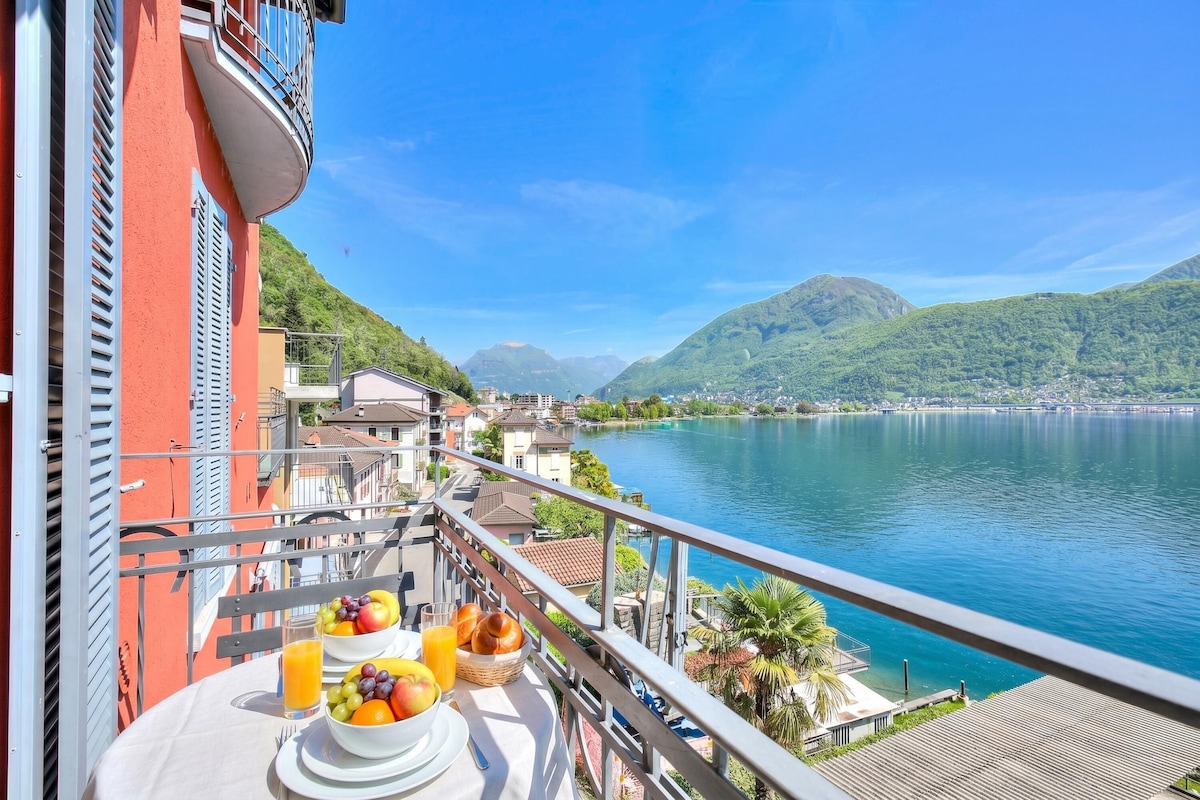 A balcony with a table set for breakfast, overlooking a lake and mountains.