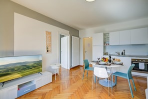 A modern kitchen with white cabinets, a dining table with chairs, and a flat-screen TV on a stand. - 76 The Lake House (Melide)
