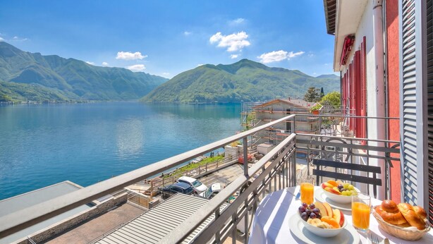 A balcony with a table set for breakfast, overlooking a lake and mountains. - 76 The Lake House (Melide)