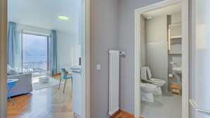 A modern apartment with a living area, a balcony, a bathroom with a toilet and sink, and a radiator. - 76 The Lake House (Melide)
