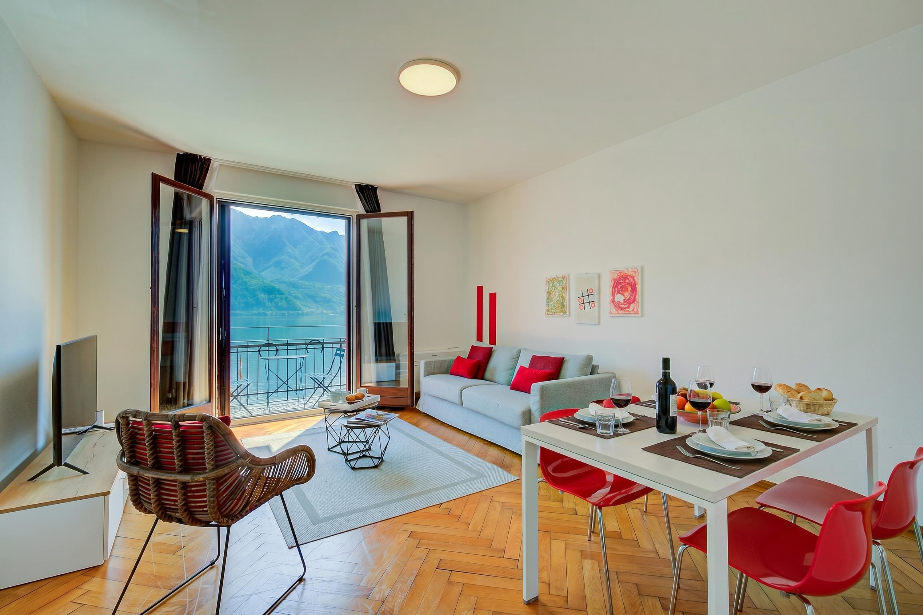 A modern living room with a sofa, dining table, and chairs, a TV, and a balcony with a mountain view.