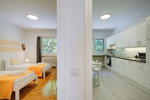 A modern hotel room with two beds, a kitchenette, and a view of trees through the window. - 76 The Lake House (Melide)