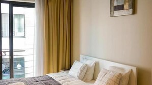 Hotellihuone, jossa on sänky, ikkuna verhoilla, taulu seinällä ja näkymä ulos.