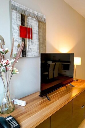 A flat-screen TV on a wooden counter, a vase with flowers, and a wall-mounted artwork. - Garden Botanique Apartment (Brussels)