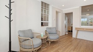 A room with two wicker chairs, a small round table, a coat rack, a window with blinds, and a wooden floor.