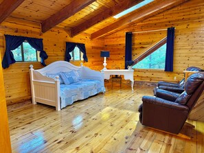 A wooden cabin interior with a bed, a desk, and a leather chair.