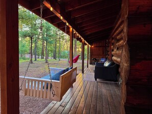 A wooden porch with a swing, a cushioned bench, and a sofa.