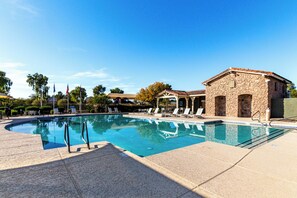 A swimming pool with lounge chairs, a stone building, and flags. - A Maricopa Must: 4BR/3BA Immaculate Home w/Jacuzzi (Maricopa)
