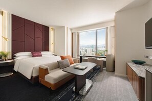 Een hotelkamer met een bed, een bank, een tafel en uitzicht op de stad.
