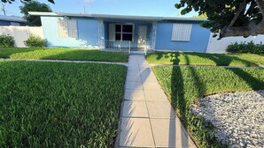 Una casa con entrada pavimentada, césped y un árbol en primer plano.