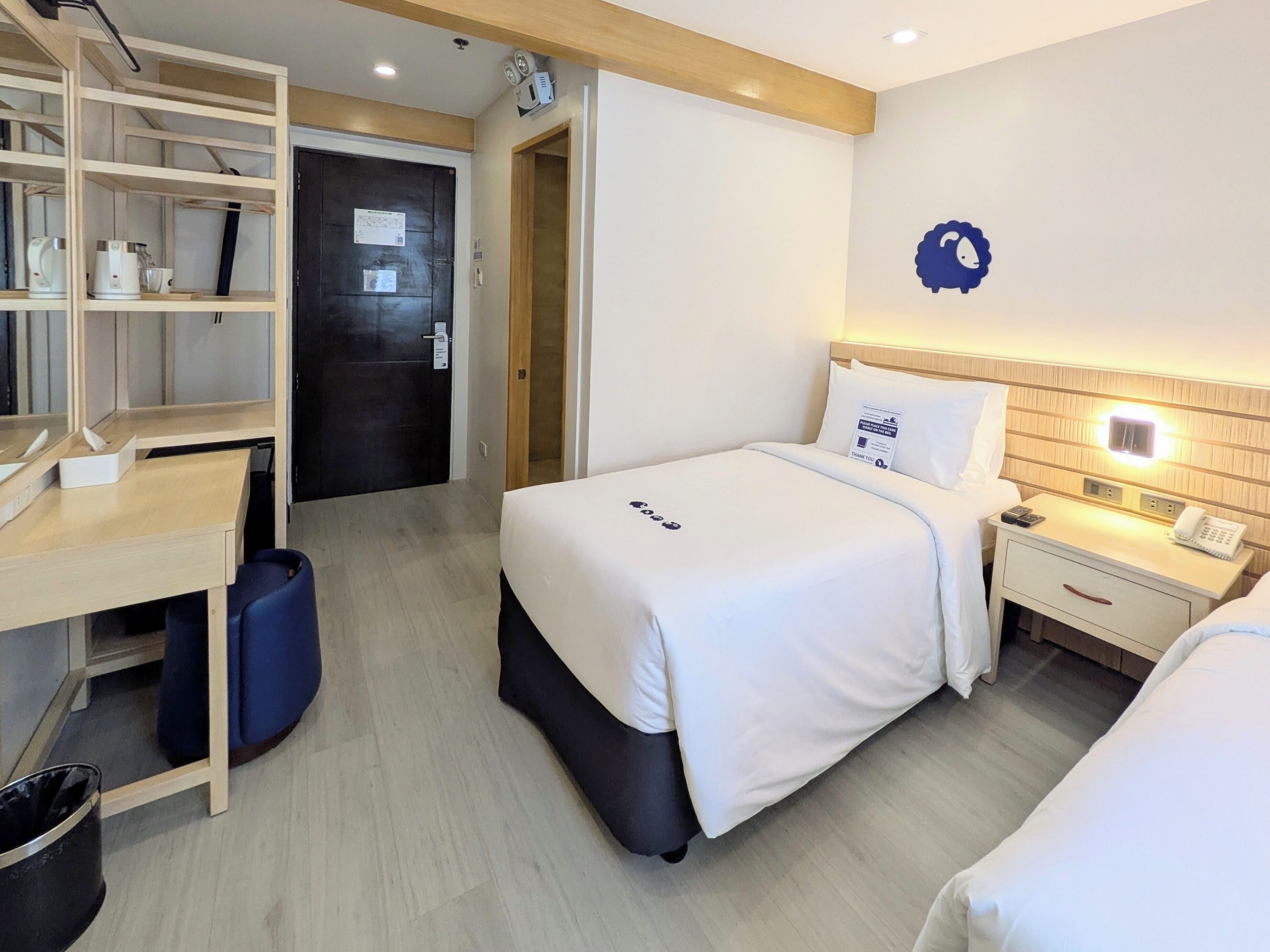 Een hotelkamer met een bed, nachtkastje, bureau en planken.