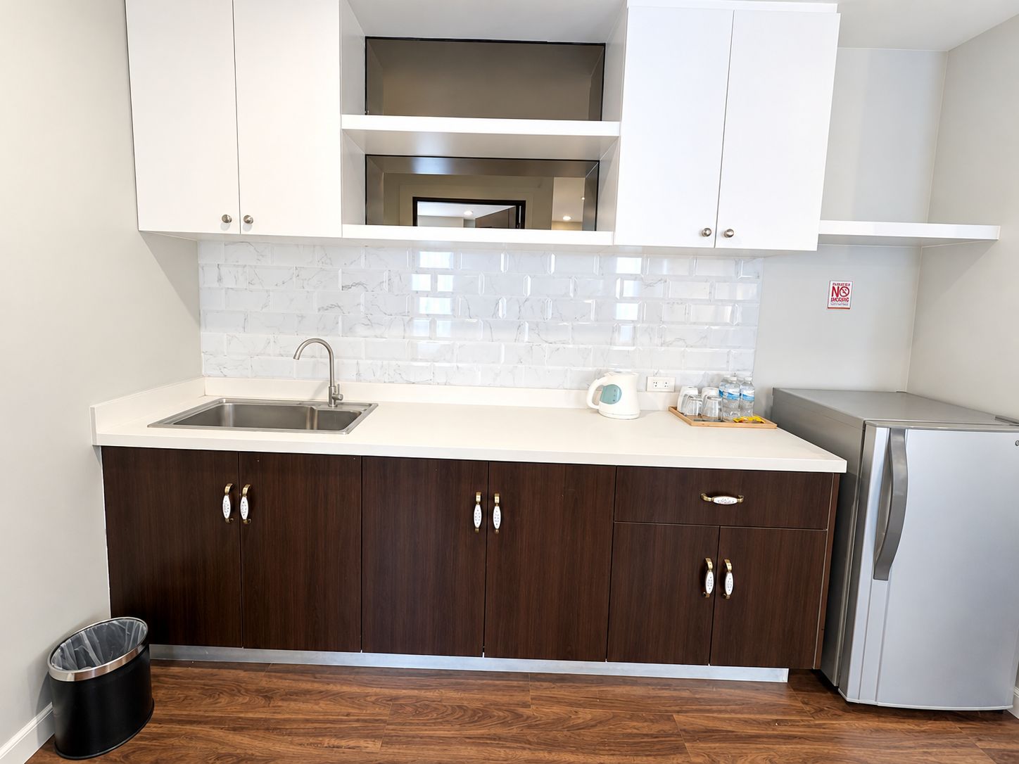 Una cucina moderna con lavello in acciaio inossidabile, pensili in legno scuro, piano di lavoro bianco e forno integrato.