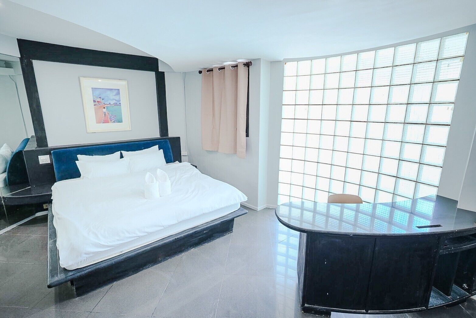 A hotel room with a bed, a desk, a window with a view, and a painting on the wall.