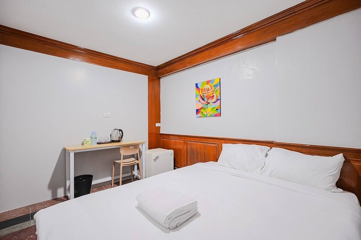 A hotel room with a bed, a desk, a chair, a radiator, and a painting on the wall.