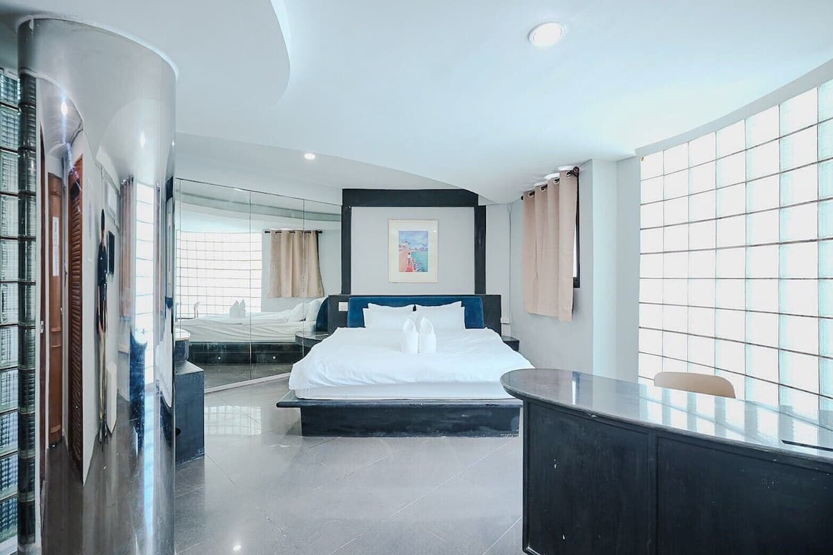 A modern hotel room with a large bed, a desk, and a view through a glass wall.