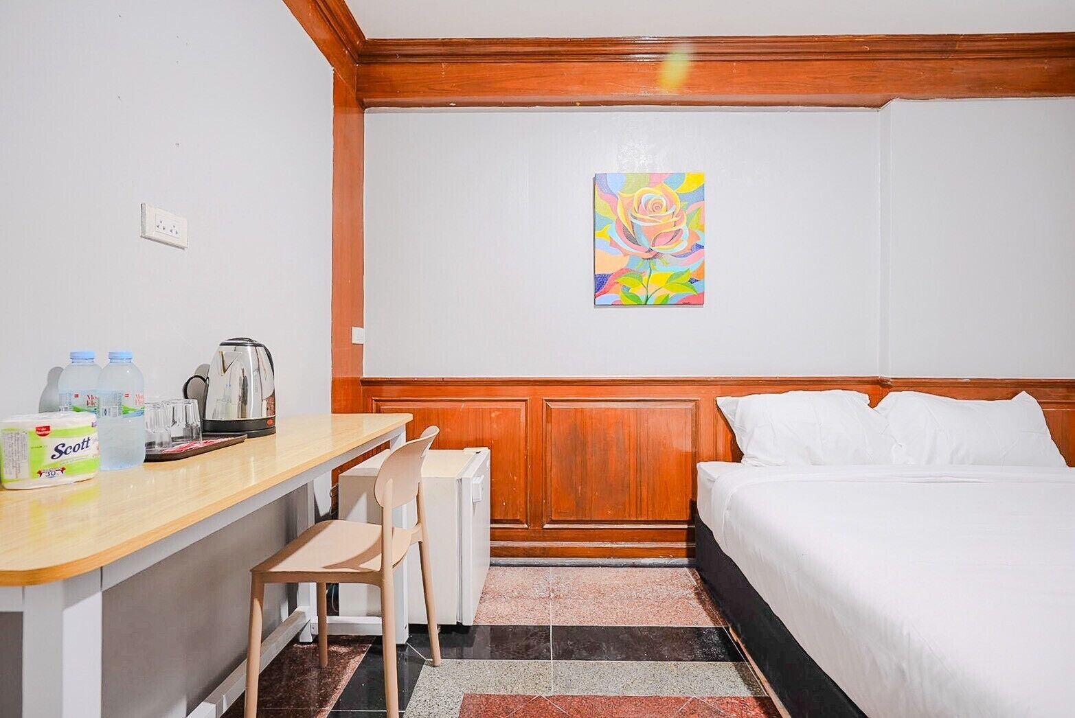 A hotel room with a bed, a desk with a chair, a coffee maker, a kettle, and a painting on the wall.