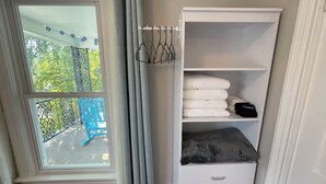 Une pièce avec une fenêtre, un balcon, un meuble de rangement blanc doté de tiroirs et un porte-vêtements suspendu.