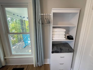 Ein Zimmer mit Fenster, Balkon, weißem Stauraum mit Schubladen und einer Kleiderstange.