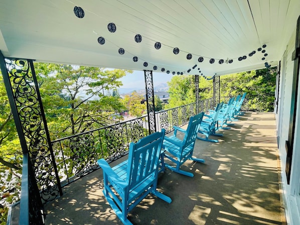 Un espace extérieur abrité, doté de chaises bleues, de guirlandes lumineuses décoratives et offrant une vue sur les arbres et les bâtiments.